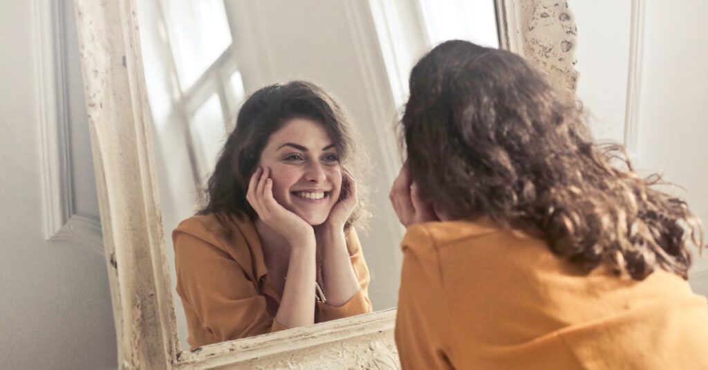A cheerful woman smiles at her reflection in a vintage-style mirror, exuding positivity and warmth.